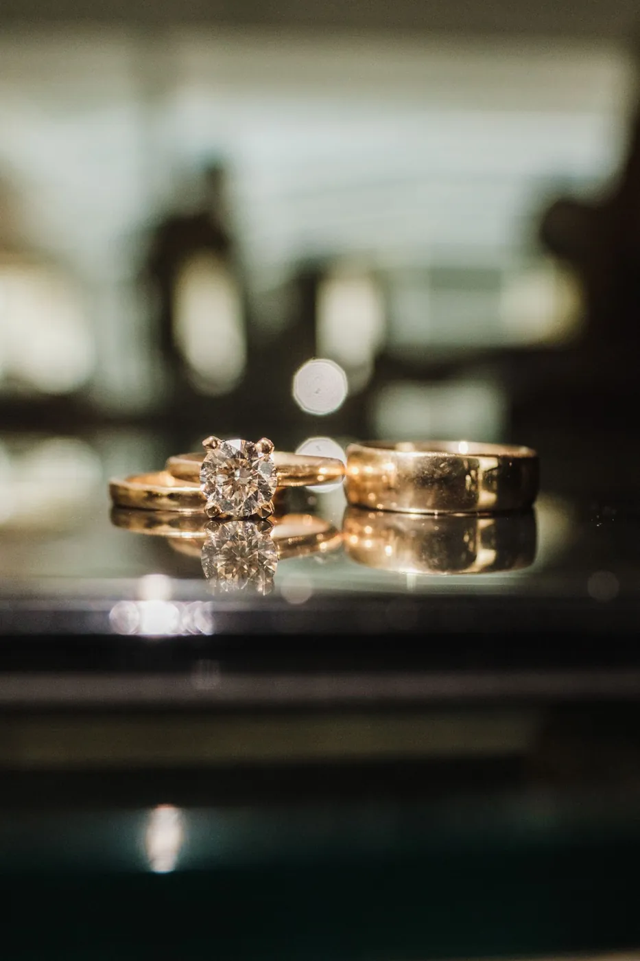 A stunning close-up of elegant gold and diamond rings on a reflective glass surface, capturing timeless love and commitment. Licensed inspiration image; not a BMG client portfolio claim.